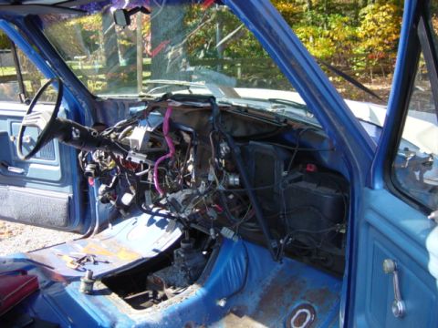 1985 Ford F-250 - The interior of a blue truck is shown with the dashboard disassembled, revealing a complex wiring system.