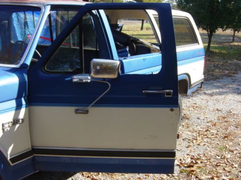 1985 Ford F-250 - A blue and cream Ford F-250 truck with the driver's door open, parked outdoors on a gravel surface.