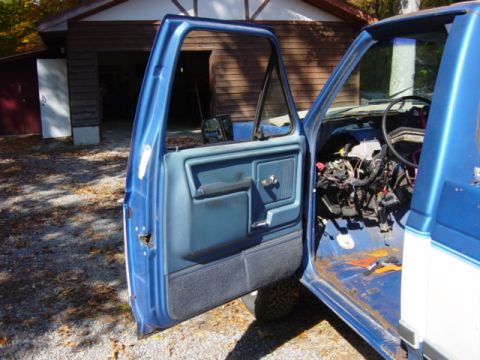1985 Ford F-250 - Driver's side door open on a 1985 Ford F-250, revealing exposed dashboard wiring and interior.