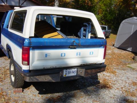 1985 Ford F-250 - Rear view of a white and blue Ford Bronco II with a blue stripe, loaded with wood in the cargo area.