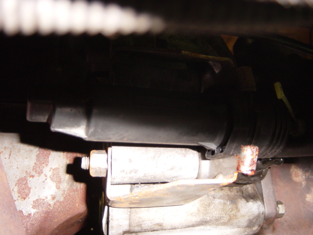 Close-up of a vehicle's exhaust pipe and mounting bracket, showing rust and a bolt
