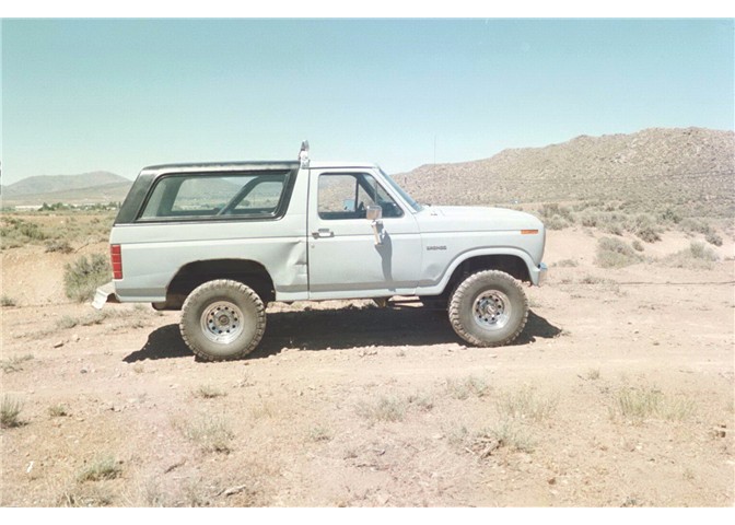 Side view of a lifted light gray Ford Bronco SUV with large off-road tires in a desert setting