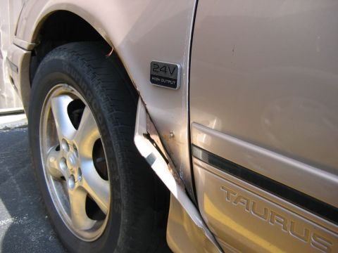1991 Ford Taurus - Close-up of a damaged tan 1991 Ford Taurus fender, revealing the model name and engine designation.