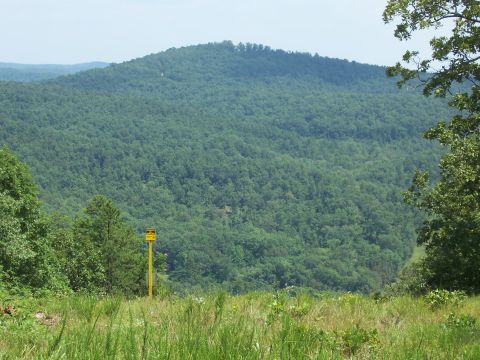 1986 Ford Bronco - A yellow sign stands in a field of grass, with a vast, forested mountain range dominating the horizon.