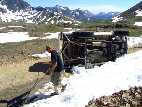 1987 Ford Bronco - A man pulls a chain next to an overturned white SUV in a snowy mountain landscape.