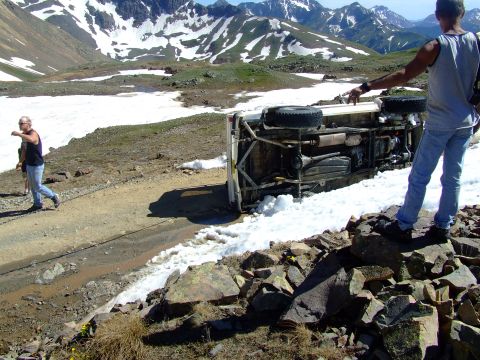 1987 Ford Bronco - SUV overturned on a mountain road, with two people observing the scene.