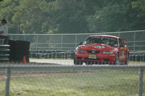 2000 Ford Mustang - A red 2000 Ford Mustang races on a track, with tires stacked along the barrier.