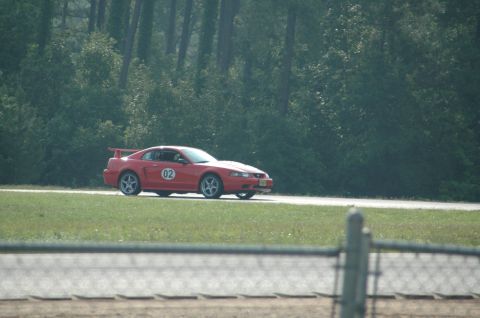 2000 Ford Mustang - A red 2000 Ford Mustang coupe, marked with racing number 02, is seen on a race track with trees in the background.