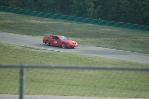 2000 Ford Mustang - A red 2000 Ford Mustang with racing decals and a spoiler is seen on a racetrack.