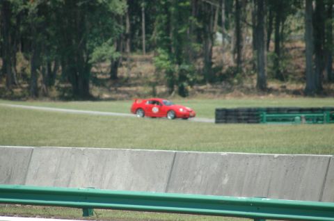 2000 Ford Mustang - A red sports car is seen on a paved track surrounded by grass and trees.