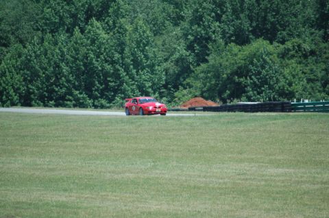 2000 Ford Mustang - Red 2000 Ford Mustang racing on a track with a wooded area behind it.