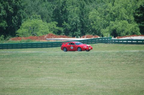 2000 Ford Mustang - A red 2000 Ford Mustang with racing number 02 drives on a grassy track with trees in the background.