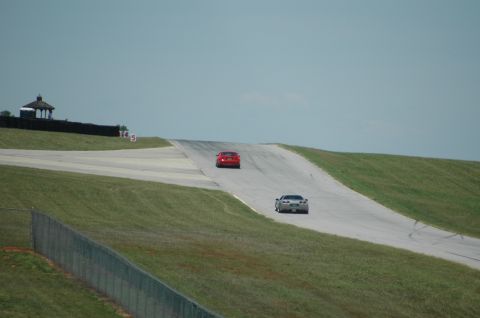 2000 Ford Mustang - Two sports cars race on a track under a clear sky, with a gazebo visible on a grassy hill.
