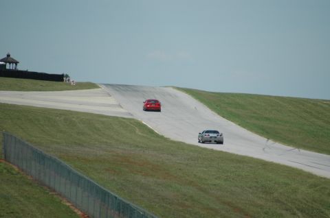 2000 Ford Mustang - Two sports cars are on a race track, one red and one silver, with a gazebo and fence visible.