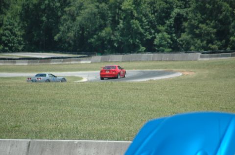 2000 Ford Mustang - A red sports car navigates a turn on a race track, with another silver vehicle visible in the distance.