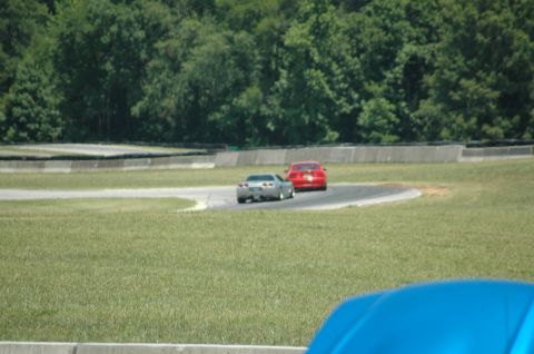 2000 Ford Mustang - Two sports cars are driving on a race track during the day.