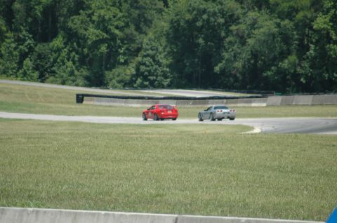 2000 Ford Mustang - Two cars are on a paved track surrounded by grass and trees.