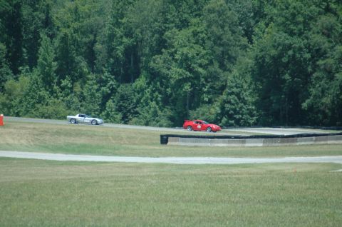 2000 Ford Mustang - Two sports cars race on a track surrounded by trees. The red car has the number 44 visible.