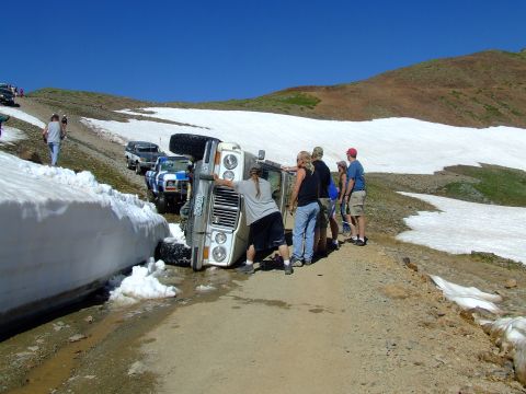 1987 Ford Bronco - A group of people try to upright a van that has rolled onto its side on a mountain road.