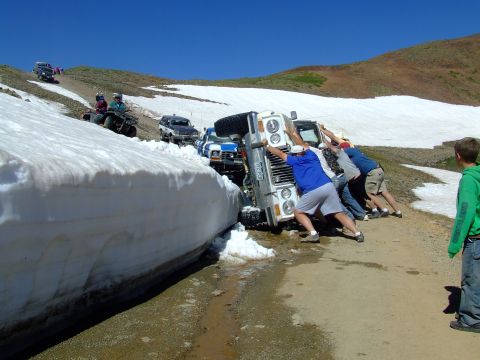 1987 Ford Bronco - A group of people push a white 1987 Ford Bronco out of a large snowbank on a mountain road.