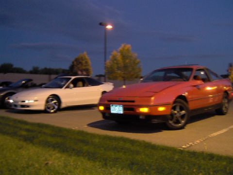 1996 Ford Probe - Two coupes are parked in a lot as the sky darkens. The red car has a license plate that reads 135 JGU.