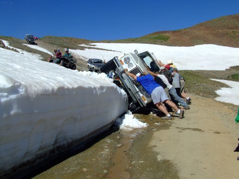 1987 Ford Bronco - Several people help push a white 1987 Ford Bronco out of a large snowbank on a mountain road.