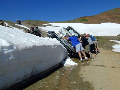 1987 Ford Bronco - Off-roaders push a Jeep out of a large snow bank on a mountain pass.