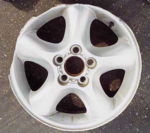 White five-spoke alloy wheel with worn paint, no tire, leaning on pavement