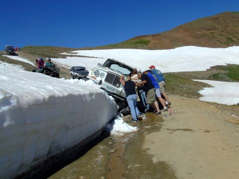 1987 Ford Bronco - A group of people work together to free a Jeep that has become stuck in a large snowdrift on a mountain pass.