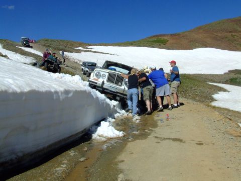 1987 Ford Bronco - Several people attempt to free a white Jeep CJ-7 that has slid into a snowbank on a mountain road.