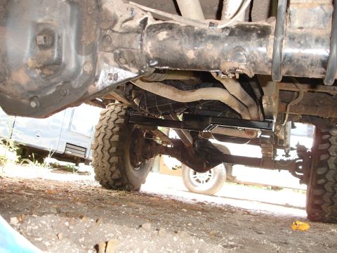 1989 Ford Bronco - A view of the undercarriage, focusing on the drivetrain and exhaust system, with another vehicle in the background.