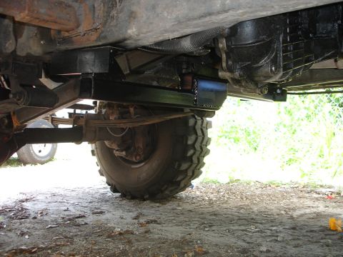 1989 Ford Bronco - The underside of a vehicle displays a custom crossmember and transmission assembly, with a large tire visible.