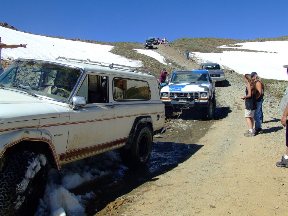 White SUV with red stripe, off-road, with snow patches on the ground
