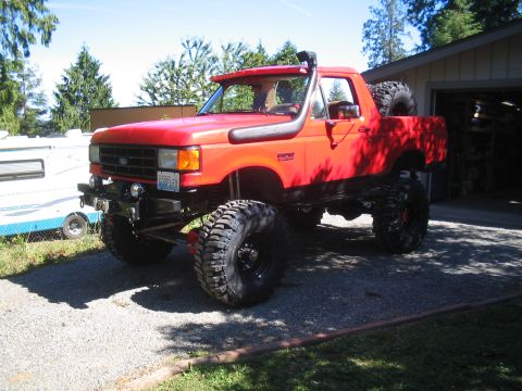 1989 Ford Bronco - This modified Ford Bronco features a snorkel and oversized tires, parked outside a garage.