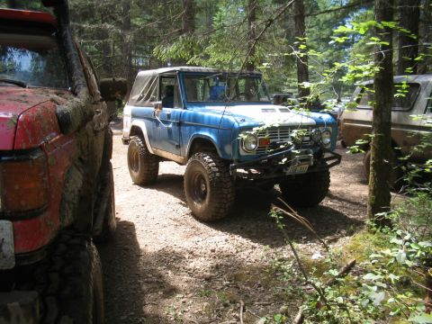 1989 Ford Bronco - First-gen Ford Bronco parked on a dirt trail, with other off-road vehicles nearby.