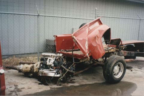 1967 Ford F-100 - The severely damaged chassis of a red pickup truck is visible, with its engine and transmission detached.