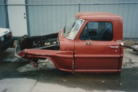 1967 Ford F-100 - The front clip of a red 1967 Ford F-100 is heavily damaged and missing its hood and engine.