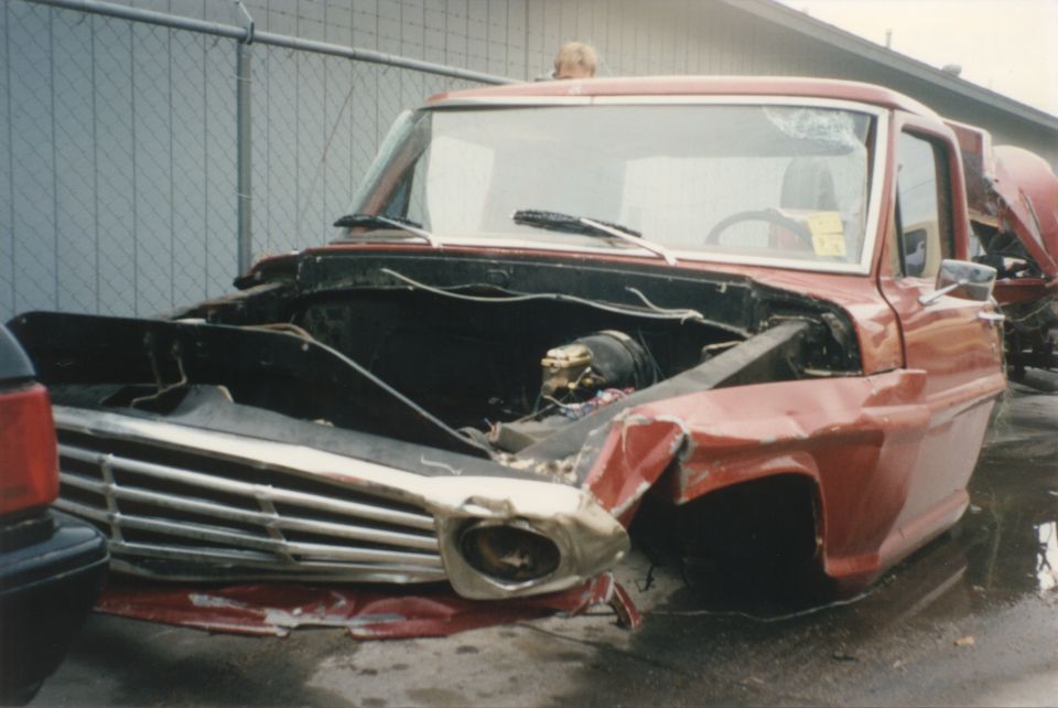 Front end of a red pickup truck with its hood open and front fender damaged