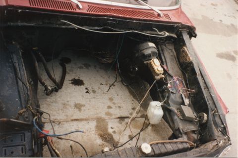 1967 Ford F-100 - The engine bay of a red vehicle shows a disconnected brake booster and master cylinder, with various wires and hoses exposed.