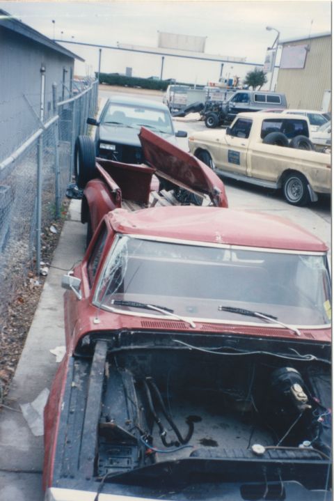 1967 Ford F-100 - Two pickup trucks are parked side-by-side, with the front of the red truck showing its engine bay.