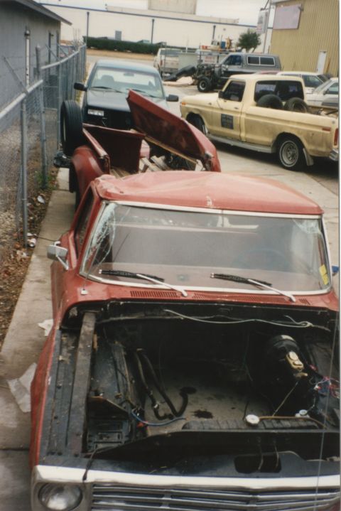 1967 Ford F-100 - A red pickup truck sits in a yard with its hood open and windshield damaged, alongside other vehicles.