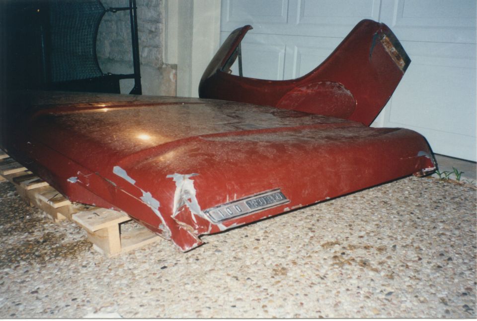 Red truck hood and fender sitting on a pallet. Badge reads 'F-100'