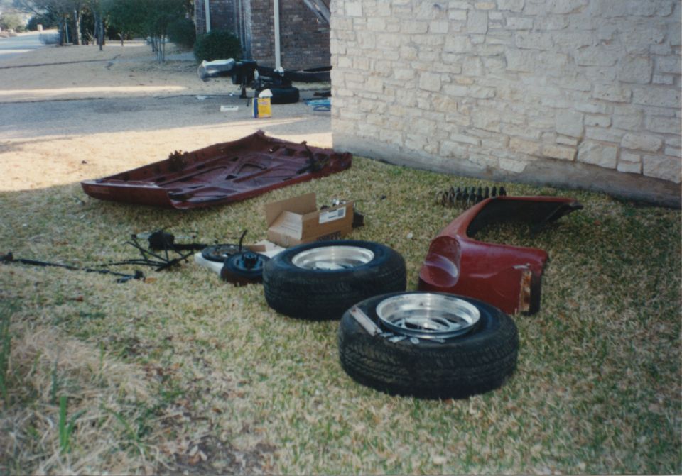 Car parts including a frame, fender, and tires laid out on grass