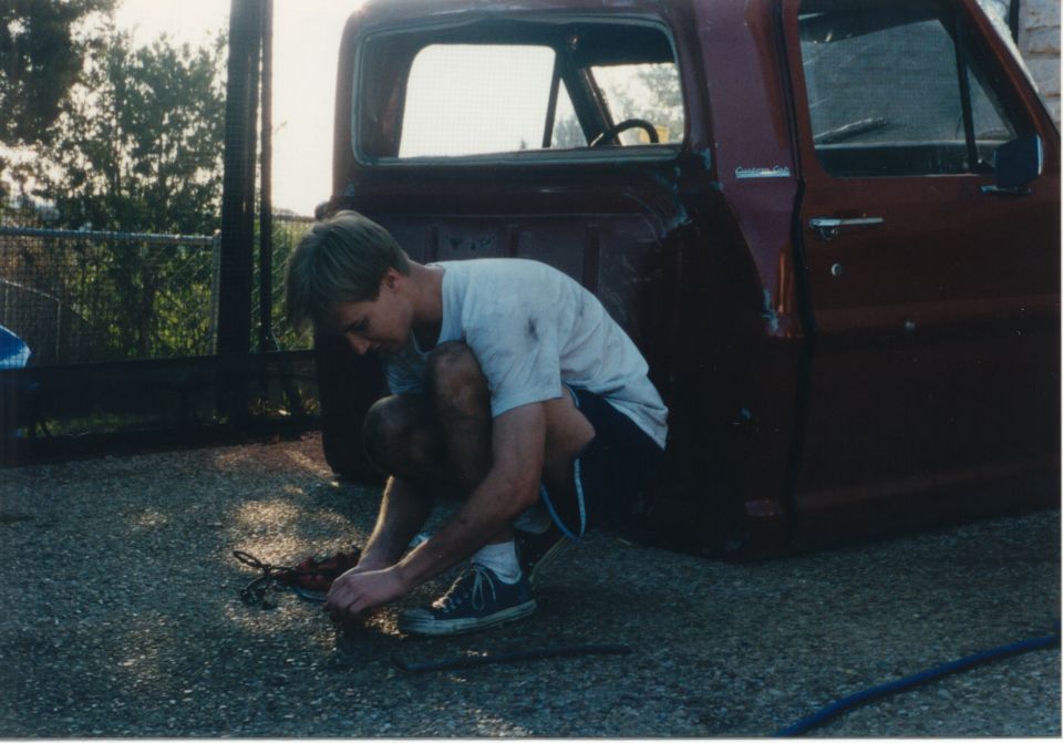 Side view of a maroon 1967 Ford F-100 pickup truck with a man working on it