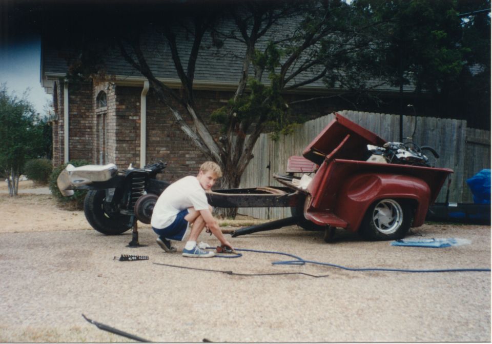 Red 1956 Ford F-100 pickup bed and chassis with a person working on it