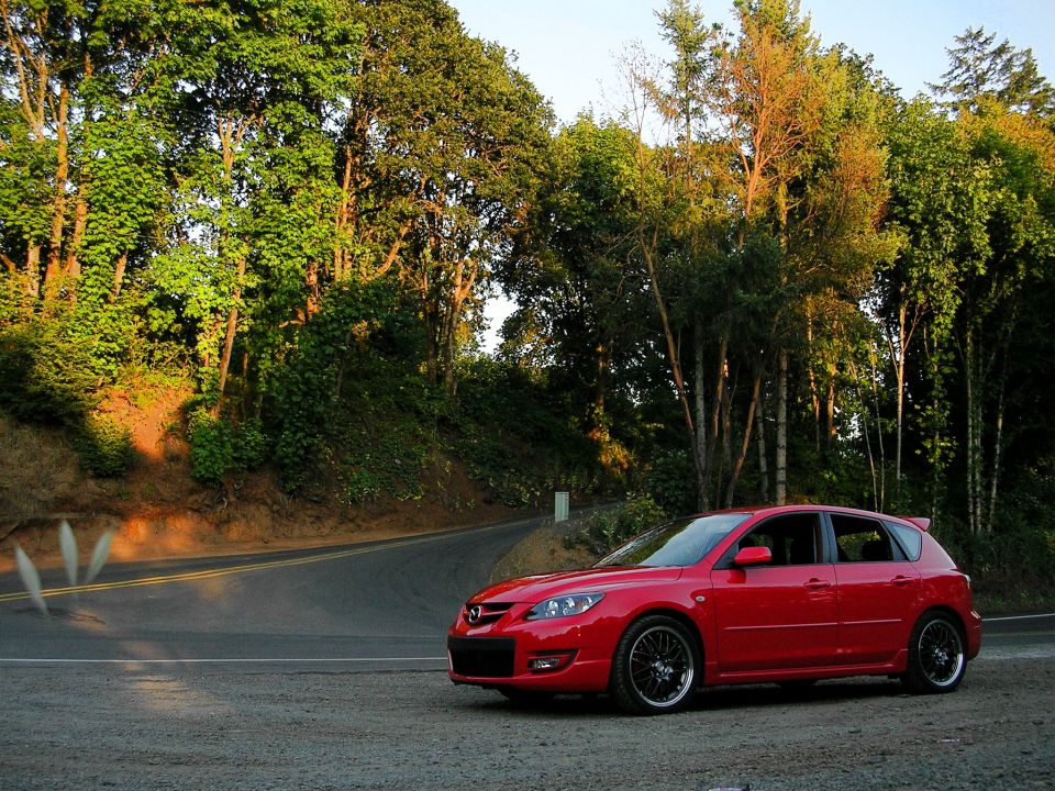 Red 2007 Mazda 3 hatchback parked on a gravel shoulder