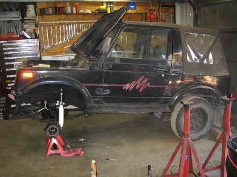 1987 Suzuki Samurai - A black 1987 Suzuki Samurai is shown with its hood up and front wheel removed, supported by jack stands in a garage.