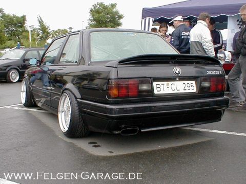 1989 BMW 3 Series - Rear view of a modified black 1989 BMW 325i, custom wheels and a spoiler, parked outdoors.