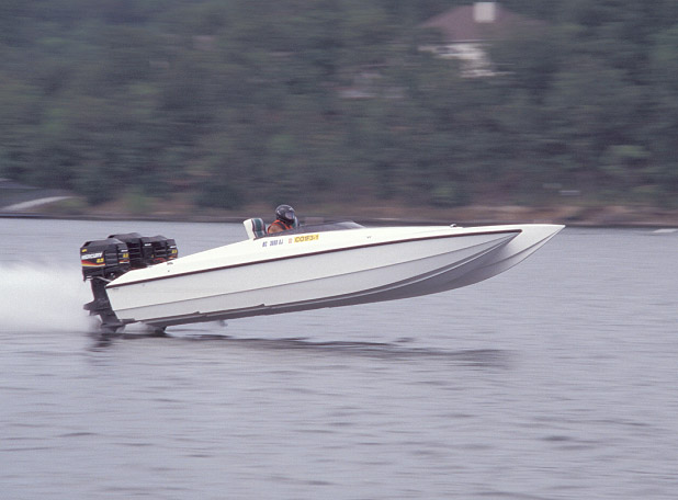 White twin-outboard performance boat running at speed with bow lifted on a lake