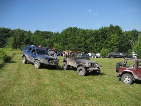 1991 Ford Bronco - Multiple off-road vehicles are gathered in a grassy field under a clear blue sky.